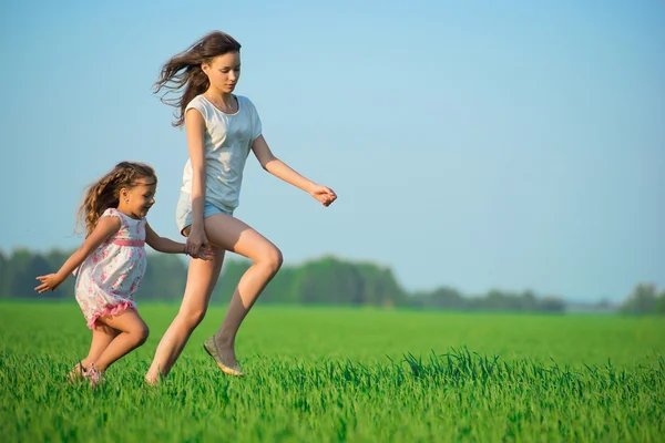 Ragazze che corrono lungo il campo di grano verde — Foto Stock