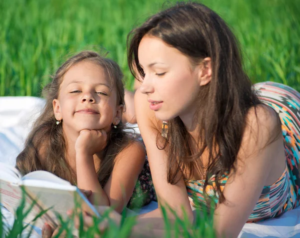 Happy girls reading book on green grass — Stock Photo, Image