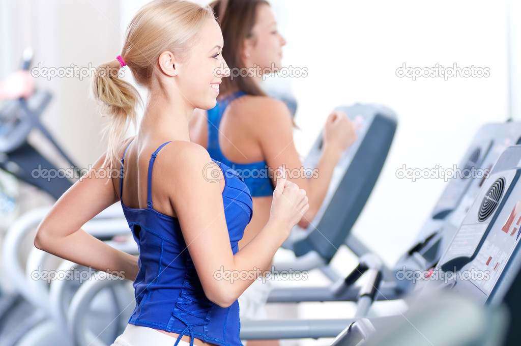 Two young women run on machine in the gym