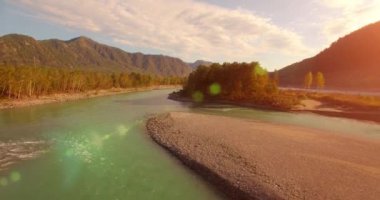 4k UHD hava görüntüsü. Güneşli yaz sabahında taze soğuk dağ nehri üzerinde alçak uçuş. Horisont 'ta yeşil ağaçlar ve güneş ışınları