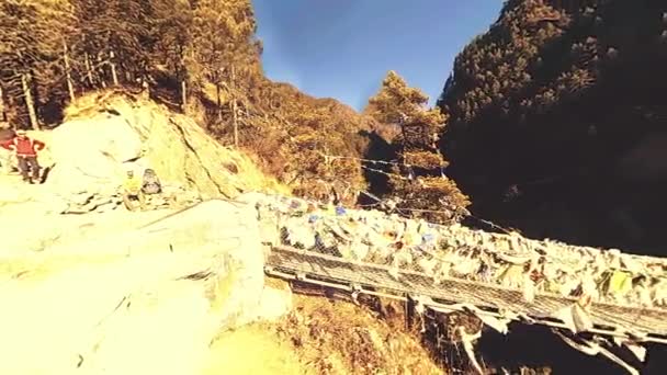 Größte Hängebrücke im Khumbu-Tal mit bunten tibetischen Gebetsfahnen. Wilde Himalaya-Hochgebirgsnatur und Bergtal. Felsige Hänge mit Bäumen bedeckt. Basislager des Everest-Gipfels. — Stockvideo