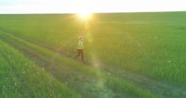 Sportif çocuk yeşil buğday tarlasında koşuyor. Kırsal çayırlarda akşam sporu alıştırmaları. Mutlu bir çocukluk sağlıklı bir yaşam biçimidir. Radikal hareket, güneş ışınları ve ot.