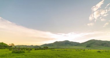 Yaz ya da sonbahar gündoğumu saatlerinde dağdaki çayır zaman atlaması. Vahşi doğa ve kırsal alan. Bulutlar hareket ediyor, yeşil çimenler ve güneş ışınları.