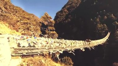 Khumbu vadisindeki en büyük asma köprü renkli Tibet dua bayraklarıyla. Vahşi Himalayalar yüksek irtifa doğa ve dağ vadisi. Ağaçlarla kaplı kayalık yamaçlar. Everest Zirvesi 'nin ana kampı..