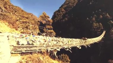 Khumbu vadisindeki en büyük asma köprü renkli Tibet dua bayraklarıyla. Vahşi Himalayalar yüksek irtifa doğa ve dağ vadisi. Ağaçlarla kaplı kayalık yamaçlar. Everest Zirvesi 'nin ana kampı..