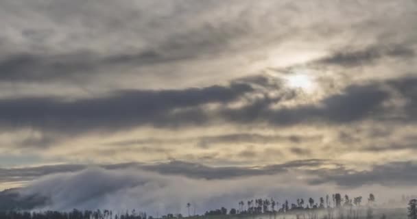 Timelapse de rayos del sol de la tarde que emergen a través de las nubes de niebla fría en las montañas. Puesta de sol en la niebla. — Vídeos de Stock