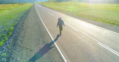 Asfalt yolda yürüyen otostopçu turist üzerinden uçuş. Yaz günü büyük bir kırsal vadi. Sırt çantalı gezgin..