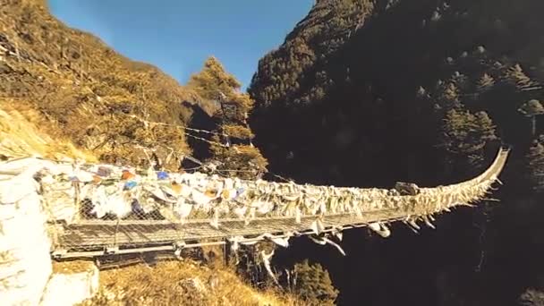Η μεγαλύτερη κρεμαστή γέφυρα στην κοιλάδα Khumbu με πολύχρωμες Θιβετιανές σημαίες προσευχής. Άγρια Ιμαλάια σε μεγάλο υψόμετρο φύση και την κοιλάδα του βουνού. Βραχώδεις πλαγιές καλυμμένες με δέντρα. Βάση στρατόπεδο του Everest κορυφή trek. — Αρχείο Βίντεο