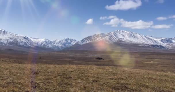 Timelapse de movimiento del sol en el cielo cristalino con nubes sobre la cima de la montaña de nieve. Hierba amarilla en el prado de altura de otoño. Naturaleza salvaje sin fin. — Vídeos de Stock