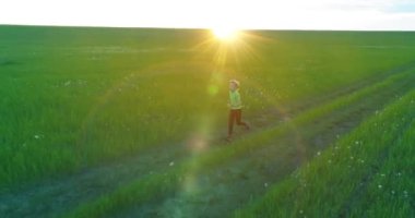 Sportif çocuk yeşil buğday tarlasında koşuyor. Kırsal çayırlarda akşam sporu alıştırmaları. Mutlu bir çocukluk sağlıklı bir yaşam biçimidir. Radikal hareket, güneş ışınları ve ot.