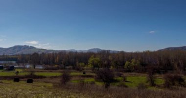 Sonbahar günbatımında çayır zamanı. Vahşi doğa ve çim tarlasında kırsal samanlıklar. Akşam sisi, güneş ışınları ve ağaçlar. Motorlu doli kaydırıcı