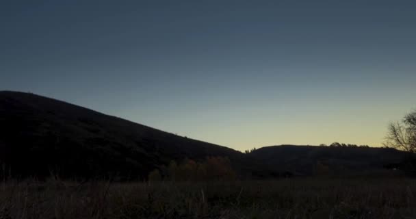 Mountain meadow time-lapse at the summer or autumn sunrise time. Wild nature and rural field. Clear sky, trees, green and yellow grass, sun rays on horizont. Motorised slider movement. — Stock Video