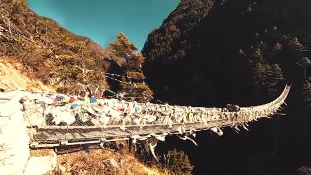 Grootste hangbrug in de Khumbu vallei met kleurrijke Tibetaanse gebedsvlaggen. Wild Himalaya 's hoge hoogte natuur en berg vallei. Rotsachtige hellingen bedekt met bomen. Basiskamp van de Everest piek trek. — Stockvideo