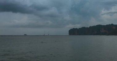 Kumsalda ve teknelerle deniz manzarasında yağmur bulutları hızlanıyor. Okyanusta tropik fırtına.
