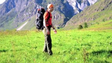 Sırt çantası ile yeşil dağ çayır üzerinde yürüyen adam hiking. Yaz spor ve eğlence kavramı.