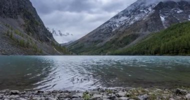 4K UHD dağ gölü zaman ayarlı yaz veya sonbahar saatlerinde. Vahşi doğa ve kırsal dağ vadisi. Çam ağaçlarından oluşan yeşil orman ve gökyüzünde hızlı bulutlar. Motorlu doli kaydırma hareketi
