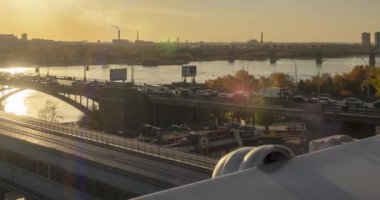 Şehir hayatının 4K UHD zaman çizelgesi. Güneş ışınları, mavi gökyüzü, ufukta nehir ve köprü. Yaz günbatımında trafik sıkışık. Motorlu kaydırma hareketi
