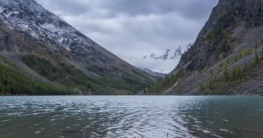 4K UHD dağ gölü zaman ayarlı yaz veya sonbahar saatlerinde. Vahşi doğa ve kırsal dağ vadisi. Çam ağaçlarından oluşan yeşil orman ve gökyüzünde hızlı bulutlar. Motorlu doli kaydırma hareketi