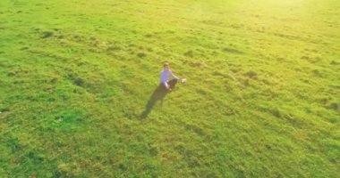 Havadan bakış açısı. Yeşil çimlerde oturan ve kırsal alanda not defteri olan bir adamın etrafında alçak yörünge uçuşları. Günlük giysi ve zen meditasyon pozu. Güneş ışınları. Radikal hareket.