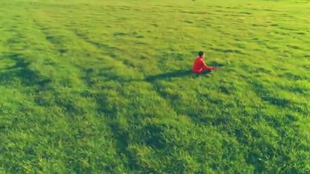 Uhd 4K航空ビュー 完璧な緑の芝生でスポーツヨガの男の上に低高度放射線飛行 山の中の夕日 地平線に緑の牧草地や太陽の光線 高速軌道運動 — ストック動画