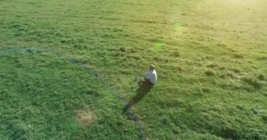 Havadan bakış açısı. Yeşil çimlerin üzerinde oturan, sarı kırsal alanda not defteri olan ve telefonla konuşan bir adam. Günlük kıyafet. Güneş ışınları. Radikal hareket.