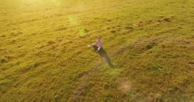 Havadan bakış açısı. Yeşil çimlerde oturan ve kırsal alanda not defteri olan bir adamın etrafında alçak yörünge uçuşları. Günlük giysi ve zen meditasyon pozu. Güneş ışınları. Radikal hareket.