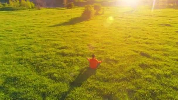 Uhd 4K航空ビュー 完璧な緑の芝生でスポーツヨガの男の上に低高度放射線飛行 山の中の夕日 地平線に緑の牧草地や太陽の光線 高速軌道運動 — ストック動画