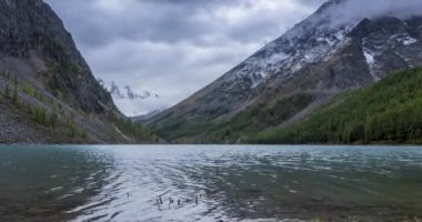 4K UHD dağ gölü zaman ayarlı yaz veya sonbahar saatlerinde. Vahşi doğa ve kırsal dağ vadisi. Çam ağaçlarından oluşan yeşil orman ve gökyüzünde hızlı bulutlar. Motorlu doli kaydırma hareketi