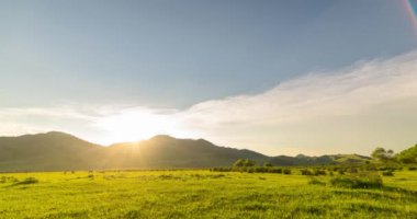 Yaz ya da sonbahar günbatımında dağdaki çayır zaman atlaması. Vahşi doğa ve kırsal alan. Bulutların hareketi, yeşil çimenler ve güneş ışınları. Motorlu Panorama