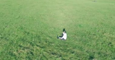 Havadan bakış açısı. Yeşil çimlerin üzerinde oturan, sarı kırsal alanda not defteri olan ve telefonla konuşan bir adam. Günlük kıyafet. Güneş ışınları. Radikal hareket.