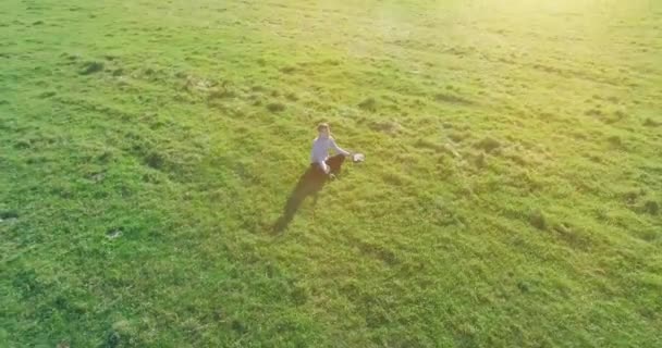空中的观点 在黄色的乡间田野 低轨道绕着人类坐在绿草上 带着记事本 随意的穿着和禅定的姿势 太阳光 拨号运动 — 图库视频影像