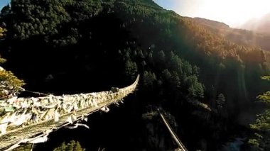 Khumbu vadisindeki en büyük asma köprü renkli Tibet dua bayraklarıyla. Vahşi Himalayalar yüksek irtifa doğa ve dağ vadisi. Ağaçlarla kaplı kayalık yamaçlar. Trek alanı ana kampa gidiyor.