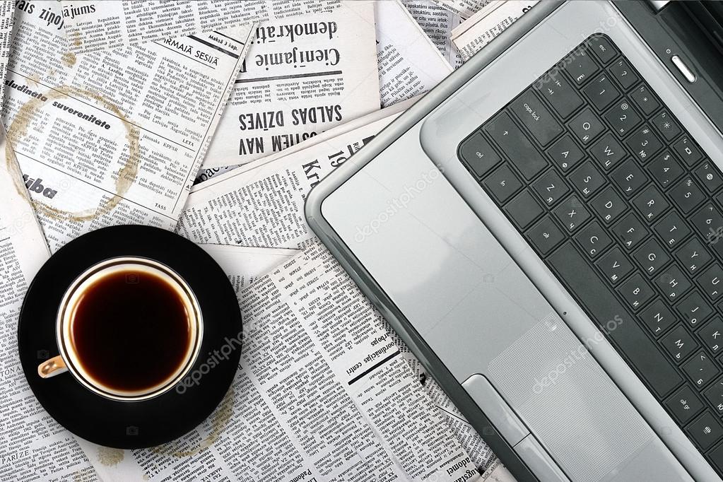 Workplace with laptop and coffee cup on newspaper background