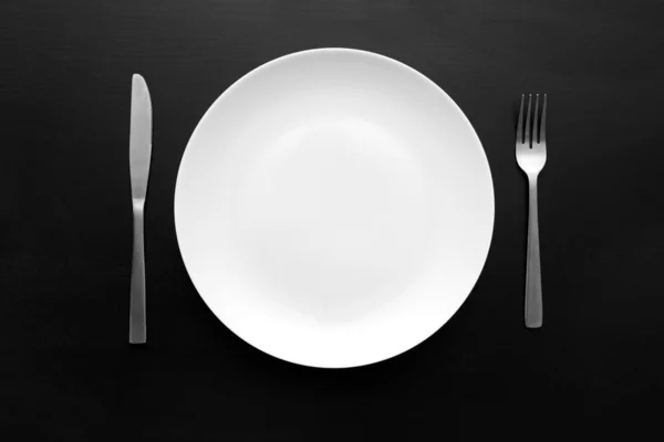 Empty white plate with fork and knife on dark wooden table — Stock Photo, Image