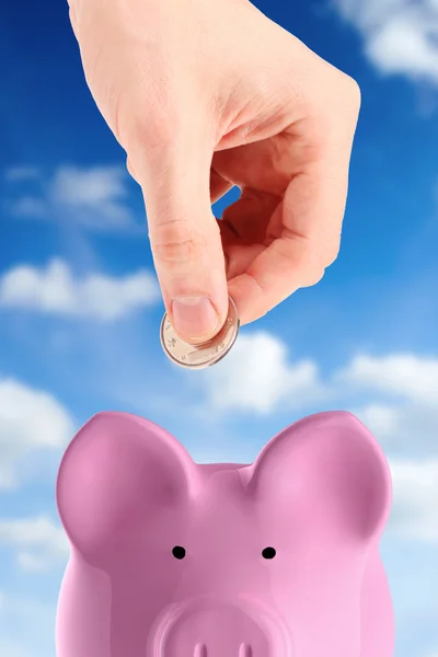 Mão colocando uma moeda no banco porquinho — Fotografia de Stock