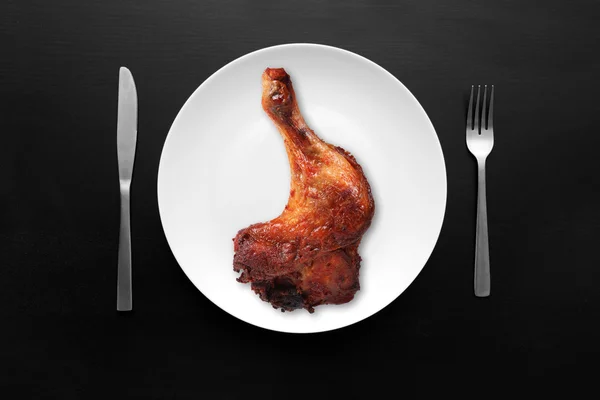 Chicken leg on white plate on dark wooden table — Stock Photo, Image