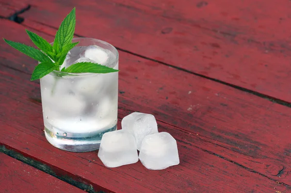 Glas vatten med isbitar och mynta på gamla träbord — Stockfoto