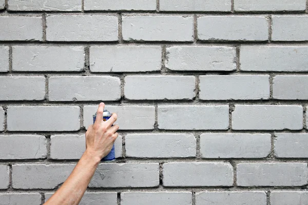 Mano con spray de graffiti puede delante de una pared de ladrillo en blanco —  Fotos de Stock