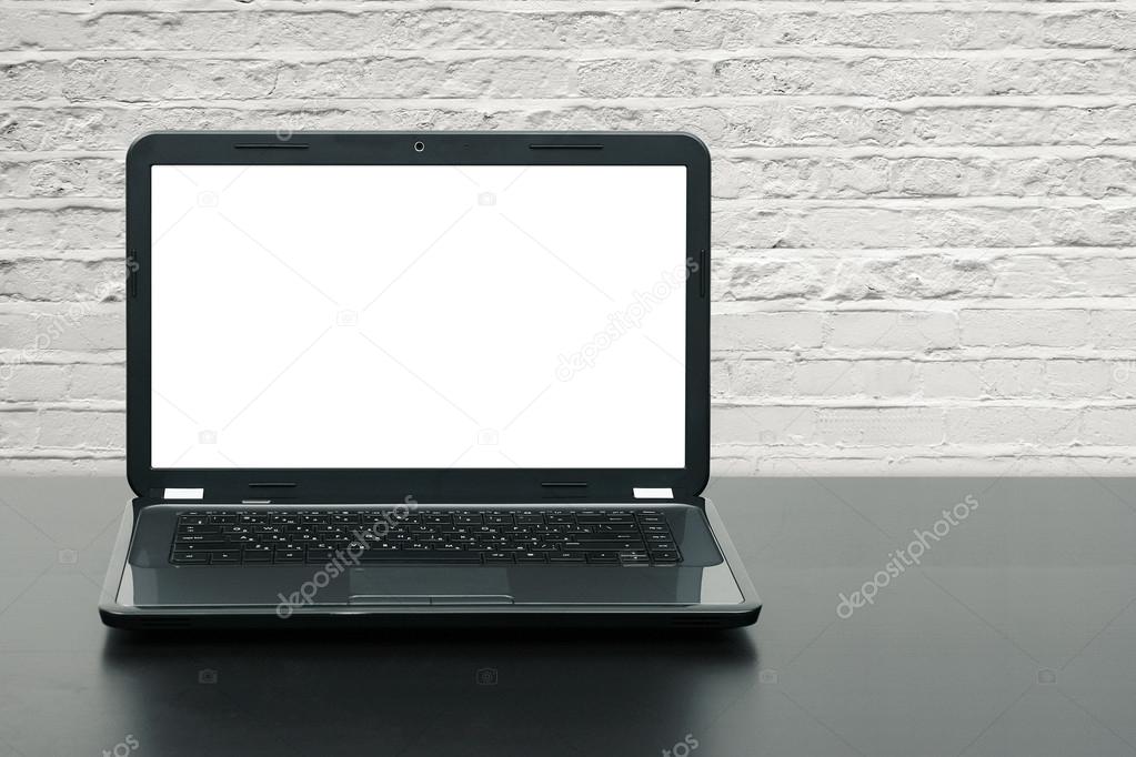 laptop with blank screen on wooden table at brick wall