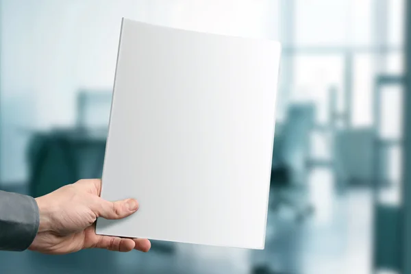 Mão segurando revista em branco com espaço de cópia no escritório — Fotografia de Stock