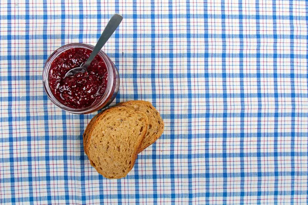 Jar with raspberry jam and sliced bread on blue tablecloth — Stock Photo, Image