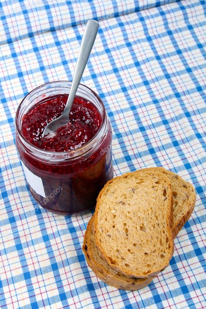 bread and jar with raspberry jam on blue tablecloth