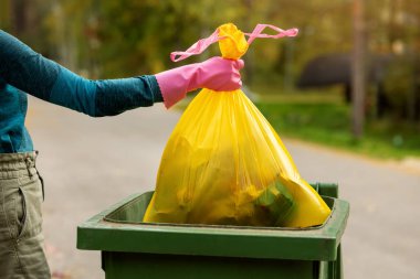El, sarı plastik bir çöp torbasını çöp kutusuna koydu. ev atıkları