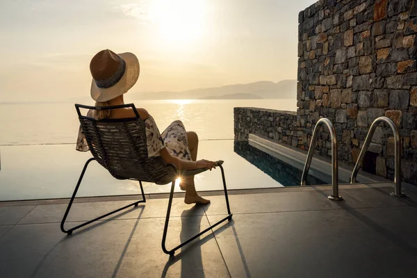 放松的度假妇女坐在游泳池前的阳台上 享受着豪华别墅的日出 — 图库照片