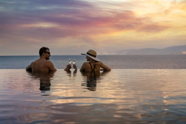 浪漫的度假胜地 情侣们在热带度假胜地的游泳池里喝着香槟 欣赏着美丽的日落 — 图库照片