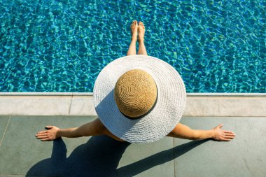 Hasır şapkalı kadın güneşleniyor ve yüzme havuzunda dinleniyor. en üstteki görünüm