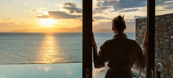 身穿浴衣的女人站在滑行的玻璃门中间 在豪华别墅里享受着大海的日出 — 图库照片