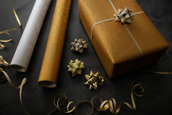 ギフトラッピング 包装紙ロールとアクセサリーで黄金のプレゼントを包んだブラックストーンの背景に — ストック写真