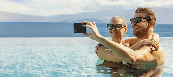 年轻快乐的夫妇带着手机在度假胜地游泳池里自娱自乐 横幅复制空间 — 图库照片