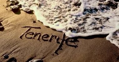 Tenerife kelimesi volkanik kumsalda okyanus dalgalarıyla silindi. yavaş çekim